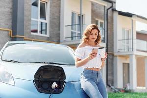 esperando a que termine la carga. mujer joven en ropa casual con su electromóvil al aire libre durante el día foto