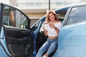 sentado en el coche. mujer joven en ropa casual con su electromóvil al aire libre durante el día foto