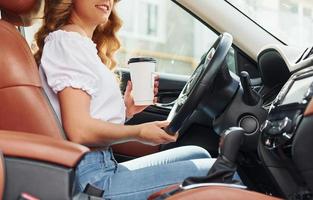 In front of steering wheel. Young woman in casual clothes is sitting in her car at daytime photo