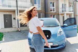 con taza de bebida. mujer joven en ropa casual con su electromóvil al aire libre durante el día foto