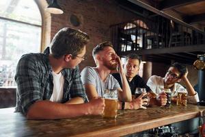 Side view of friends with beer. People in casual clothes sitting in the pub photo