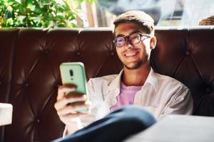 teléfono inteligente en la mano. hombre con ropa informal sentado en el pub foto