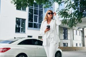 In sunglasses. Woman in formal wear standing outdoors in the city at daytime photo