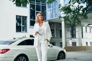 coche blanco en el fondo. mujer con ropa formal parada al aire libre en la ciudad durante el día foto