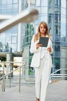 Against business building. Woman in formal wear standing outdoors in the city at daytime photo