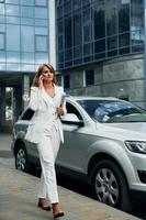 With phone in hand. Woman in formal wear standing outdoors in the city at daytime photo