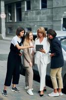 Women in formal wear is outdoors in the city together standing near silver colored car photo