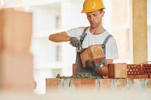 Building process. Young man working in uniform at construction at daytime photo