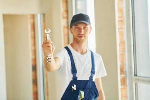 With wrench in hands. Young man working in uniform at construction at daytime photo