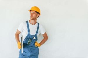 Standing near white wall. Young man working in uniform at construction at daytime photo