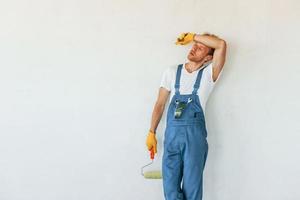 Standing against finished white walls. Young man working in uniform at construction at daytime photo