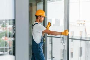 Clearing windows. Young man working in uniform at construction at daytime photo