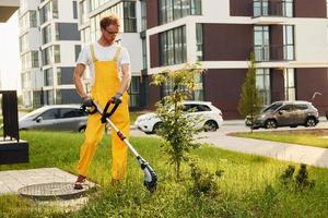 Building exterior at background. Man cut the grass with lawn mover outdoors in the yard photo