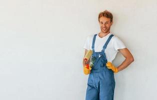 de pie contra paredes blancas acabadas. joven que trabaja en uniforme en la construcción durante el día foto