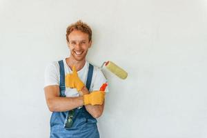 Painting the walls. Young man working in uniform at construction at daytime photo