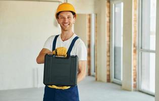 Indoors in unfinished room. Young man working in uniform at construction at daytime photo