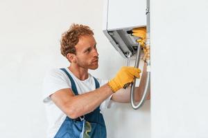 Repairing water heater. Young man working in uniform at construction at daytime photo