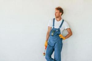 Against white walls. Young man working in uniform at construction at daytime photo