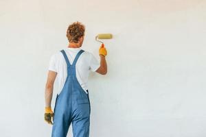 Painting the walls. Young man working in uniform at construction at daytime photo