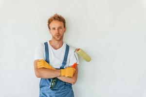 Painting the walls. Young man working in uniform at construction at daytime photo