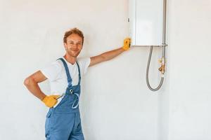 Repairing water heater. Young man working in uniform at construction at daytime photo