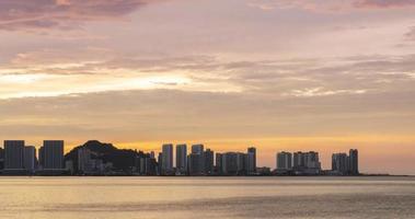 timelapse silhouet visie van waterkant stad met hoogbouw wolkenkrabber gebouw in de buurt zee kust strand terwijl zonsondergang zonsondergang tijd met vanille schemering lucht video