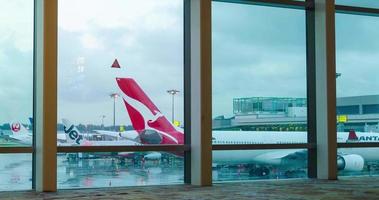 vista interior de lapso de tiempo dentro de la sala de la terminal de salida con ventana gigante con avión qantas airbus a330 y aviones de otras aerolíneas estacionados en el aeropuerto