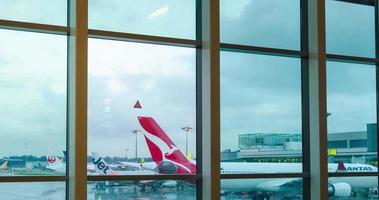 timelapse vue intérieure à l'intérieur du hall du terminal de départ avec fenêtre géante avec avion qantas airbus a330 et autres avions de compagnies aériennes se garant à l'aéroport video