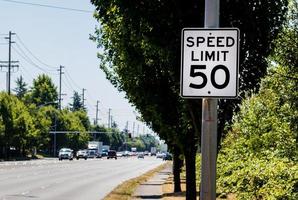 Señal de límite de velocidad de 50 mph en un puesto con una carretera y un árbol foto