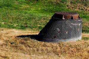 Manhole raised on a concrete rise next to brown and green grass photo