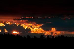 Red sunrise sunset over a tree line horizon with heavy clouds photo