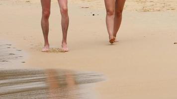 homem e mulher andando descalços na praia. feche os pés como casal no verão. férias caminhando juntos na praia video