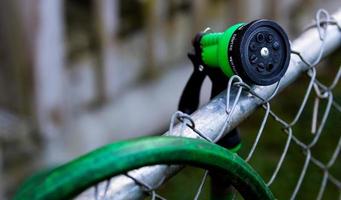 Green garden hose nozzle on a fence near photo