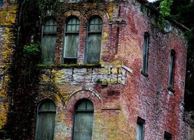 Abandoned brick 2 story building with moss and plant growth photo