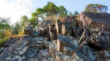 Looking up a rocky cliff with trees on the top photo
