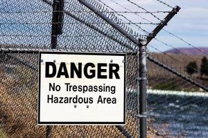 Dangerous no trespassing hazardous ares white sign on a barbed wire chain link fence photo