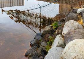 Fence submerged in tidal water with grass and debris photo