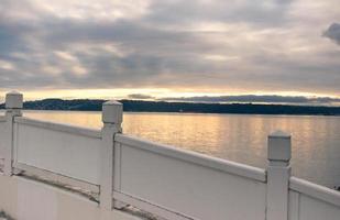 Cloudy sunrise as seen over the rail of a wooden foot bridge overlooking a harbor photo