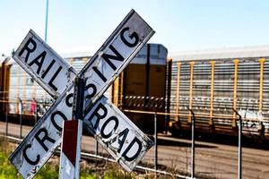 Old worn railroad crossing sign in front of a barbed wire fence and cars photo