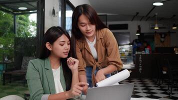 dolly sparo, giovane donna e sua femmina collega Lavorando su il computer portatile computer e carta opera o rapporto nel caffè negozio video