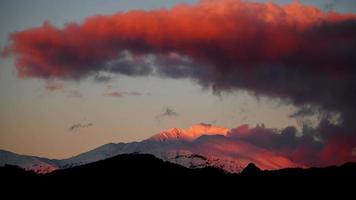 Snow-capped mountain illuminated by a pink sunset color video