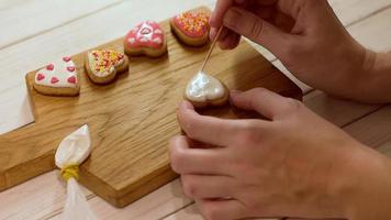 processus de décoration du pain d'épice avec du glaçage. les mains de la femme décorent des biscuits en forme de coeur pour la saint valentin video