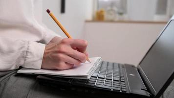 trabalho remoto. mulher faz anotações no caderno e imprime no teclado do laptop. educação a distância e conceito de e-learning video