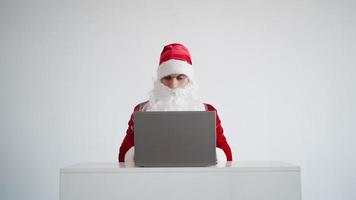 Der Weihnachtsmann tippt Text auf einer Laptop-Tastatur auf weißem Hintergrund. Weihnachten im Internet. neues Jahr 2022. video