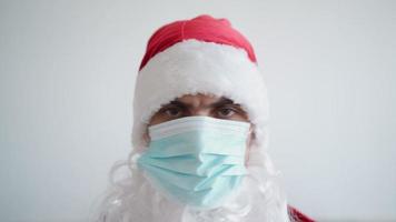 santa claus i en medicinsk mask utseende på de kamera med en allvarlig se på en vit bakgrund. jul karantän och coronavirus begrepp. ny år pandemisk. video