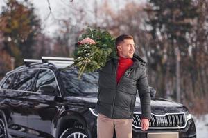 Holding green fir in hands. Man is outdoors near his car. Conception of holidays photo