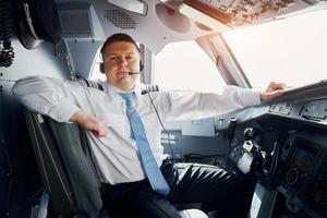 Pilot in formal wear sits in the cockpit and controls airplane photo