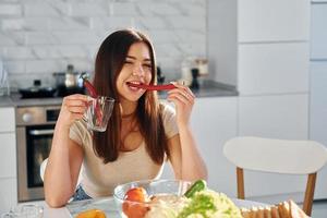 Pretty young woman in casual clothes sits on the kitchen with red pepper photo