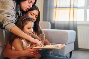 Reading book together. Female lesbian couple with little daughter spending time together at home photo