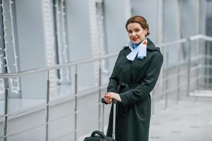 Woman passenger with luggage is outdoors near airport photo